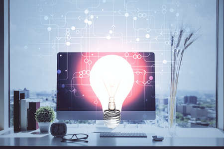 Computer on desktop in office with bulb icon hologram. Double exposure. Concept of idea.の写真素材