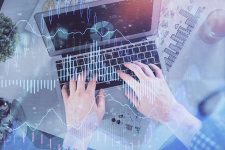 Double exposure of mans hands typing over laptop keyboard and forex chart hologram drawing. Top...