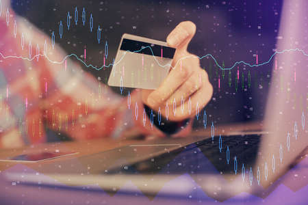 Double exposure of man hands holding a credit card and Forex graph drawing. Stock trading and digital fintech in Internet E-commerce concept.の写真素材