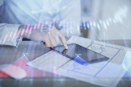 Double exposure of mans hands holding and using a digital device and forex graph drawing. Financial...