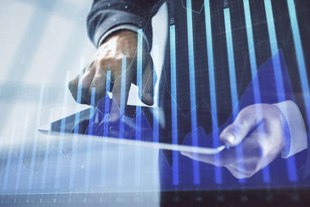 Double exposure of mans hands holding and using a digital device and forex graph drawing. Financial...