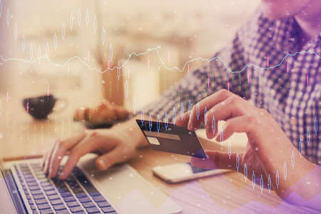 Double exposure of man hands holding a credit card and Forex graph drawing. Stock trading and...