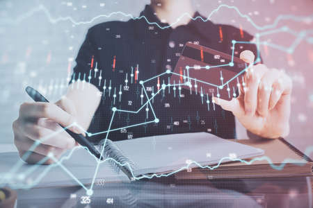 Double exposure of man hands holding a credit card and Forex graph drawing. Stock trading and digital fintech in Internet E-commerce concept.の写真素材