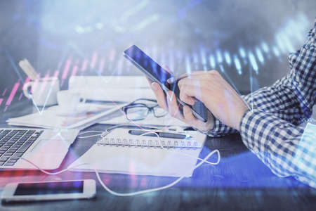 Double exposure of mans hands holding and using a digital device and forex graph drawing. Financial...