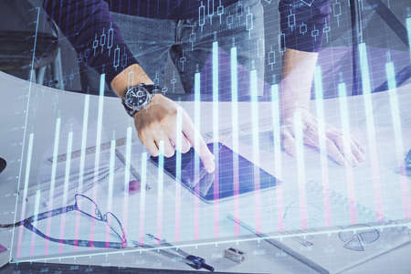 Double exposure of mans hands holding and using a digital device and forex graph drawing. Financial...