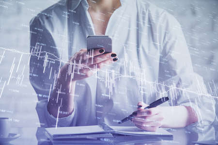 Double exposure of forex chart sketch hologram and woman holding and using a mobile device....