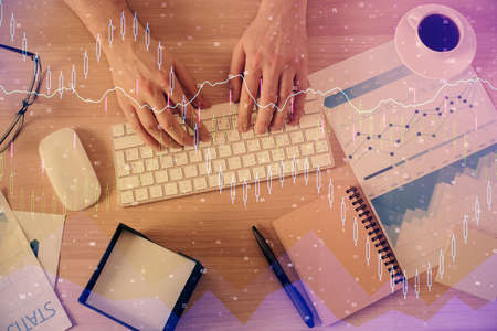 Multi exposure of mans hands typing over computer keyboard and forex graph hologram drawing. Top...