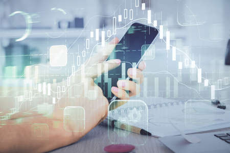Double exposure of mans hands holding and using a digital device and forex graph drawing. Financial...