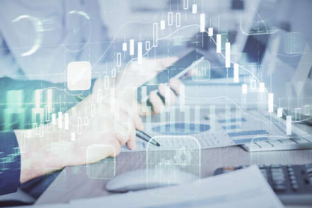 Double exposure of mans hands holding and using a digital device and forex graph drawing. Financial...