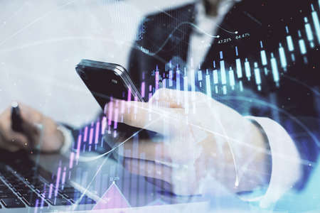 Multi exposure of mans hands holding and using a digital phone and forex graph drawing. Financial...