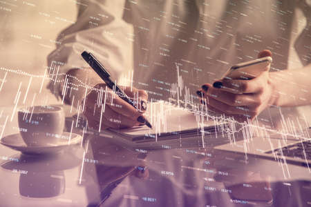 Double exposure of financial graph sketch hologram and woman holding and using a mobile device....