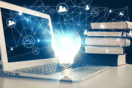 Computer on desktop in office with bulb icon hologram. Double exposure. Concept of idea.
