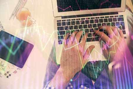 Double exposure of mans hands typing over laptop keyboard and forex chart hologram drawing. Top...