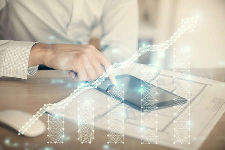 Double exposure of mans hands holding and using a digital device and forex graph drawing. Financial...