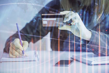 Double exposure of woman on-line shopping holding a credit card and financial graph drawing. Stock...