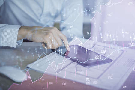 Double exposure of mans hands holding and using a digital device and forex graph drawing. Financial...