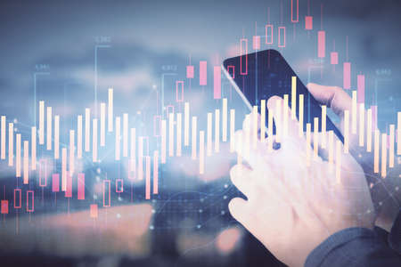 Double exposure of mans hands holding and using a digital device and forex graph drawing. Financial...