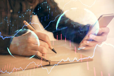 Double exposure of forex graph sketch hologram and woman holding and using a mobile device. Stock...