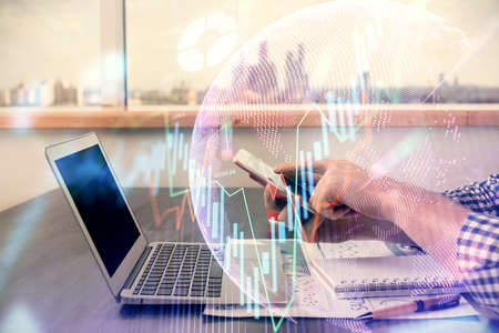 Double exposure of mans hands holding and using a digital device and forex graph drawing. Financial...