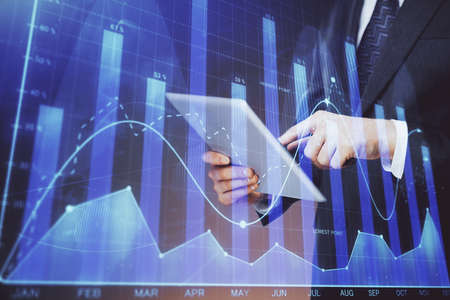 Double exposure of mans hands holding and using a digital device and forex graph drawing. Financial...