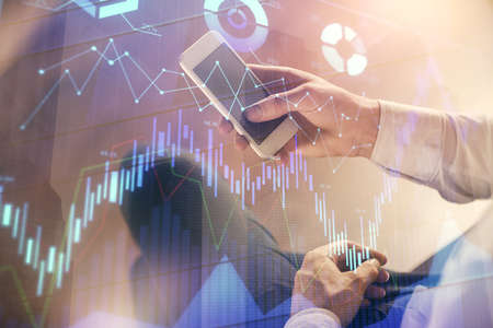 Double exposure of mans hands holding and using a digital device and forex graph drawing. Financial...
