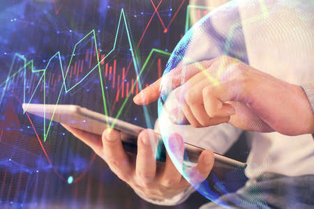 Double exposure of mans hands holding and using a digital device and forex graph drawing. Financial...