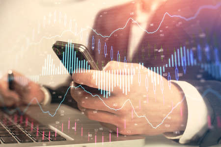 Multi exposure of mans hands holding and using a digital phone and forex graph drawing. Financial...
