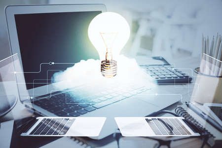Computer on desktop in office with bulb icon hologram. Double exposure. Concept of idea.
