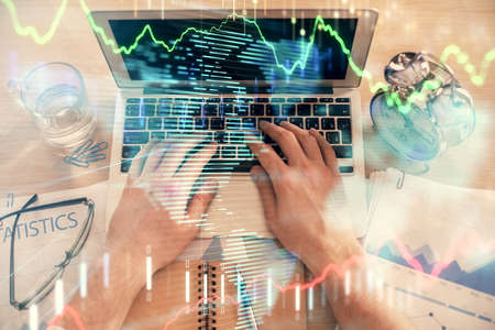 Double exposure of mans hands typing over laptop keyboard and forex chart hologram drawing. Top...