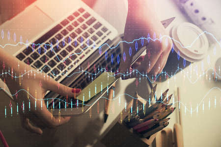 Double exposure of businesswoman hands typing on computer and financial graph hologram drawing....