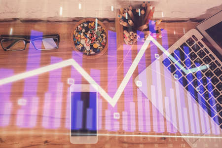 Double exposure of financial graph hologram over desktop with phone. Top view. Mobile trade platform...