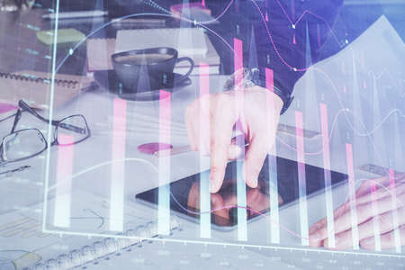 Double exposure of mans hands holding and using a digital device and forex graph drawing. Financial...