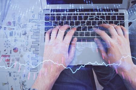 Double exposure of mans hands typing over laptop keyboard and forex chart hologram drawing. Top...