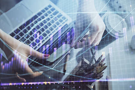 Double exposure of businesswoman hands typing on computer and financial graph hologram drawing....