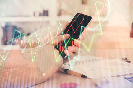 Double exposure of mans hands holding and using a digital device and forex graph drawing. Financial market concept.の写真素材