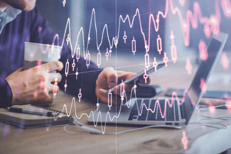 Double exposure of mans hands holding and using a phone and financial graph drawing. Analysis...