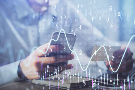 Double exposure of mans hands holding and using a phone and financial graph drawing. Analysis...