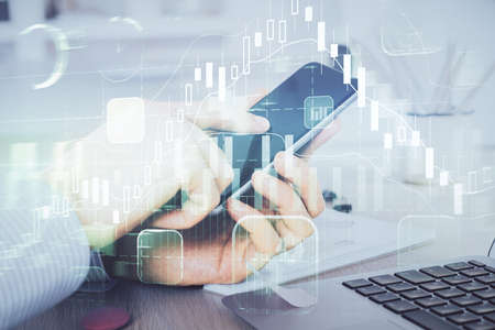 Double exposure of mans hands holding and using a digital device and forex graph drawing. Financial...