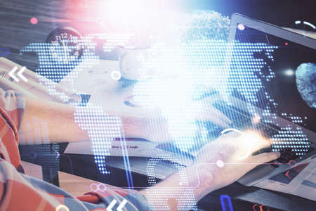 Double exposure of world map hologram with man working on computer on background. Concept of...