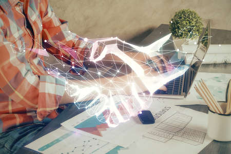 Handshake hologram drawing with businessman working on computer on background. Double exposure.の写真素材
