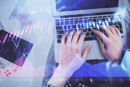 Double exposure of mans hands typing over laptop keyboard and forex chart hologram drawing. Top...