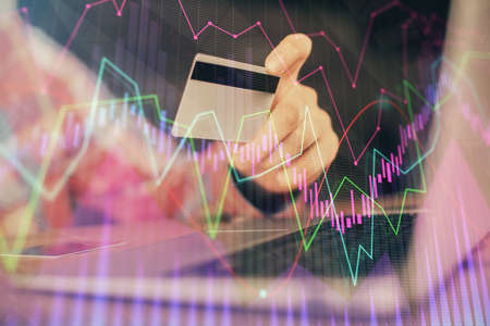 Double exposure of man hands holding a credit card and Forex graph drawing. Stock trading and...