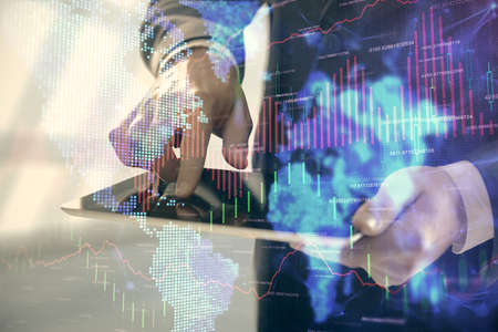 Double exposure of mans hands holding and using a digital device and forex graph drawing. Financial...