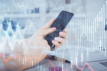 Double exposure of mans hands holding and using a digital device and forex graph drawing. Financial market concept.の写真素材