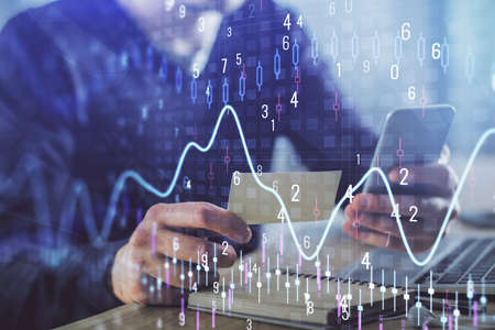 Double exposure of mans hands holding and using a phone and financial graph drawing. Analysis...