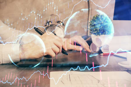 Double exposure of mans hands holding and using a phone and financial graph drawing. Analysis...