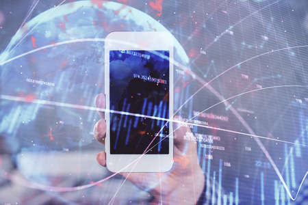 Double exposure of mans hands holding and using a digital device and forex graph drawing. Financial...