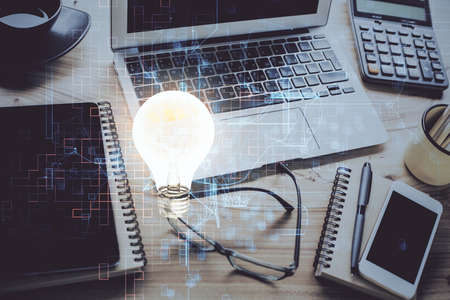 Computer on desktop in office with bulb icon hologram. Double exposure. Concept of idea.の写真素材
