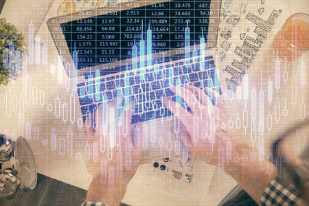 Double exposure of mans hands typing over laptop keyboard and forex chart hologram drawing. Top...