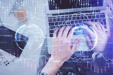 Double exposure of mans hands typing over laptop keyboard and forex chart hologram drawing. Top...